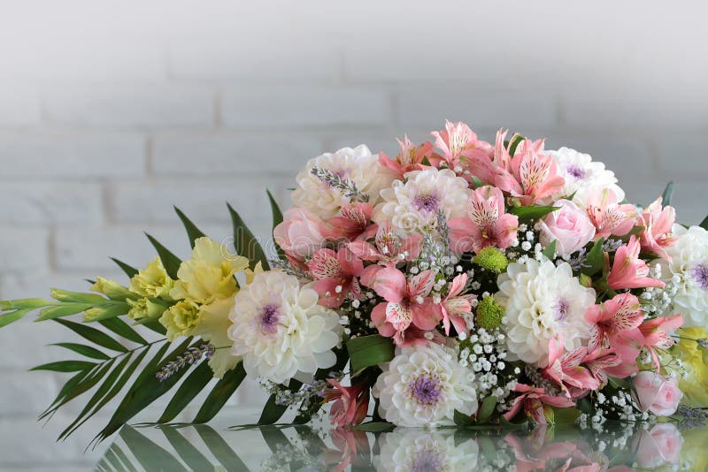 Closeup beautiful bunch of fresh tender flowers in white and rosy colores yellow gladioluses mixed decorated with green leaves lies sidelong on glass table on blurred gray background, horizontal picture. Closeup beautiful bunch of fresh tender flowers in white and rosy colores yellow gladioluses mixed decorated with green leaves lies sidelong on glass table on blurred gray background, horizontal picture