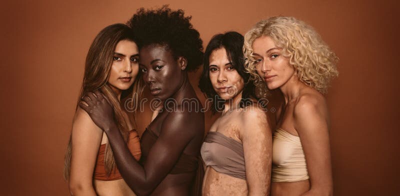 Group of diverse women standing together against brown background. Multi ethnic females looking at camera in studio. Group of diverse women standing together against brown background. Multi ethnic females looking at camera in studio.