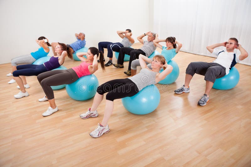 Class of diverse people doing pilates exercises in a gym doing head lifts to strengthen their abdominal muscles. Class of diverse people doing pilates exercises in a gym doing head lifts to strengthen their abdominal muscles