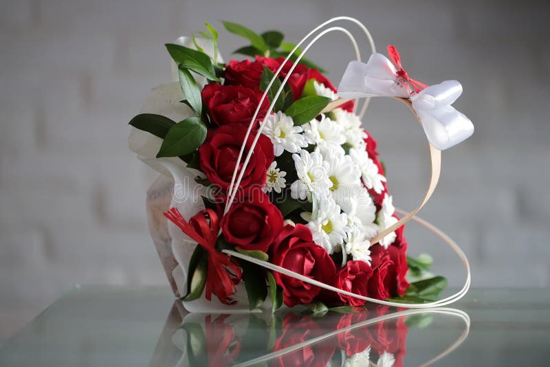 Beautiful bunch of fresh red roses white chrysanthemums decorated with green leaves bows lies sidelong on glass table on blurred gray background, horizontal picture. Beautiful bunch of fresh red roses white chrysanthemums decorated with green leaves bows lies sidelong on glass table on blurred gray background, horizontal picture