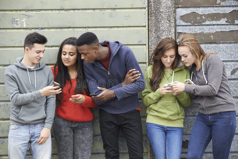 Grupp av tonåringar som delar textmeddelandet på mobiltelefoner