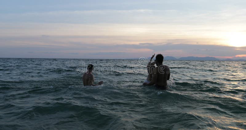 Grupp av vänner som tillsammans plaskar i havet på solnedgången, ung simning för gladlynt folk på stranden under sommarsemester arkivfilmer