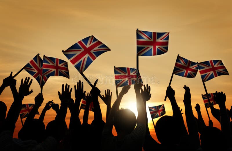 Grupp människor som vinkar UK-flaggor i tillbaka Lit royaltyfria foton Grupp människor som vinkar UK-flaggor i tillbaka Lit royaltyfria foton