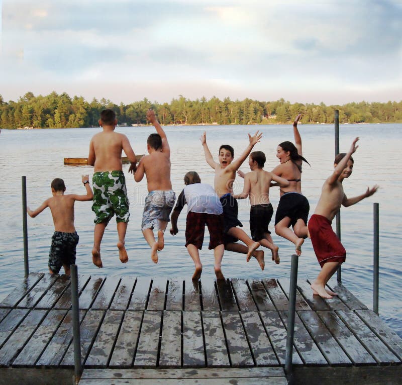 A group of eight kids ages 11-13 jumping off on a dock into a lake at summer camp. A group of eight kids ages 11-13 jumping off on a dock into a lake at summer camp.