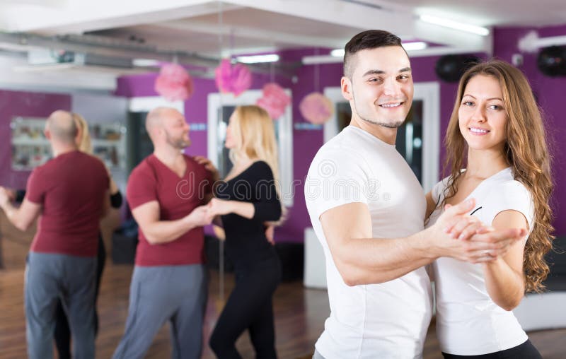 Group of smiling young adults dancing salsa at dance class. Focus on guy. Group of smiling young adults dancing salsa at dance class. Focus on guy