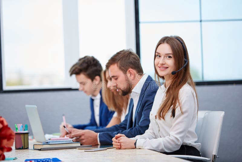 Gruppe Arbeitskräfte, die im Büro, Mädchen in den Kopfhörern betrachten Kamera und das Lächeln arbeiten stockbild Gruppe Arbeitskräfte, die im Büro, Mädchen in den Kopfhörern betrachten Kamera und das Lächeln arbeiten stockbild