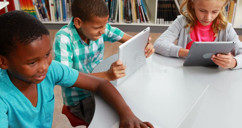 Gruppe der Schule scherzt unter Verwendung der digitalen Tablette und des Laptops in der Bibliothek