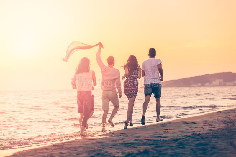 Gruppe glückliche junge Leute läuft auf Hintergrund des Sonnenuntergangstrandes und -meeres lizenzfreies stockbild Gruppe glückliche junge Leute läuft auf Hintergrund des Sonnenuntergangstrandes und -meeres lizenzfreies stockbild