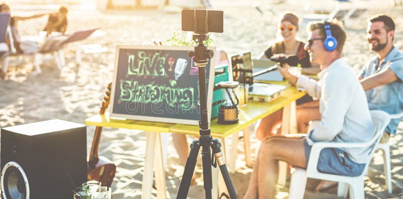 Gruppe glücklichen Menschen, die eine Videozufuhr Online am Strandfest machen- Sprecher und Freunde, die das Livesozialströmen be