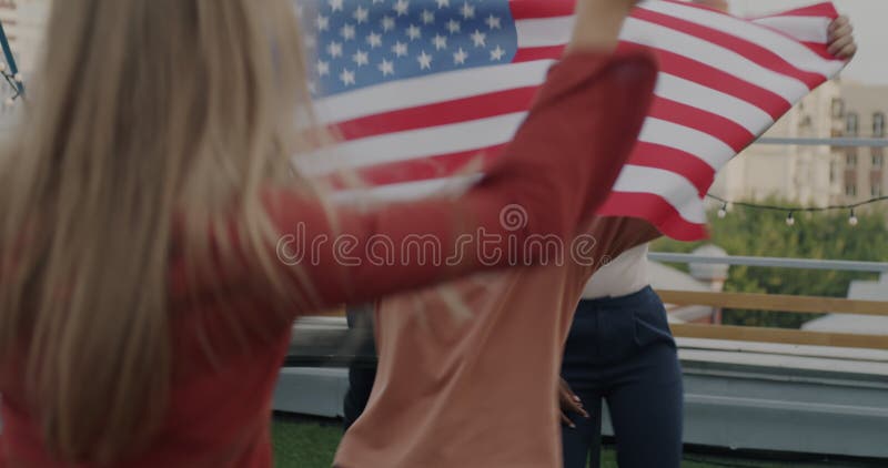 Gruppe junger Leute, die unter amerikanischer Flagge tanzen und sich auf der Dachterrasse amüsieren, um Nationalfeiertage zu feier