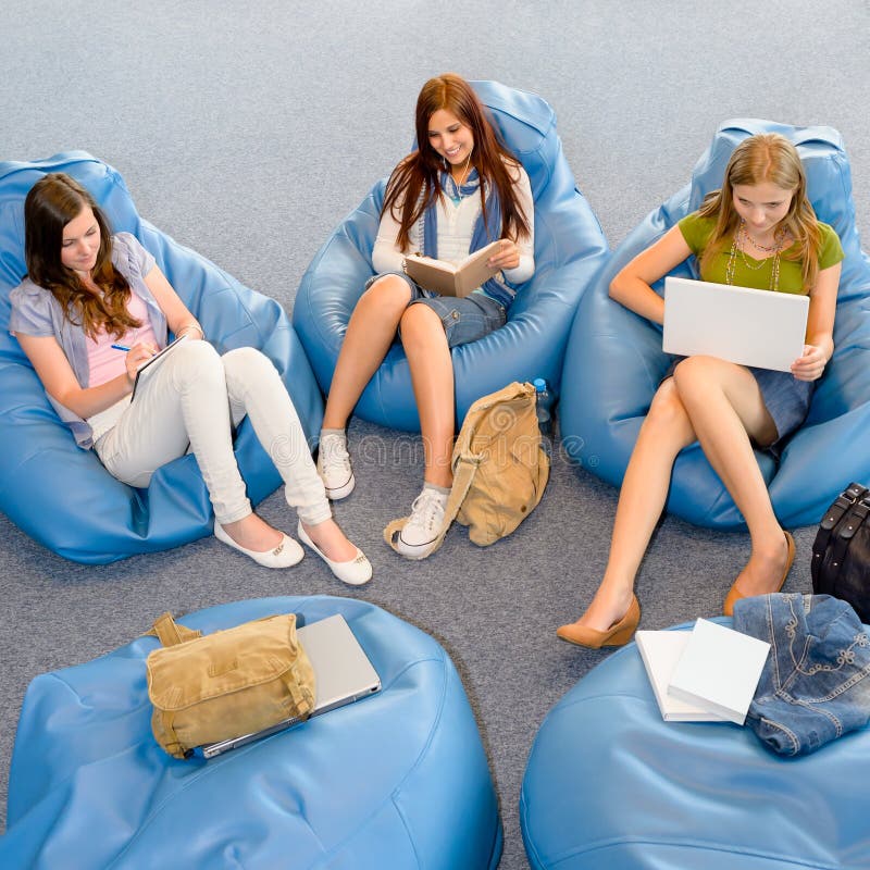 Young student girls resting on blue beanbags at library. Young student girls resting on blue beanbags at library