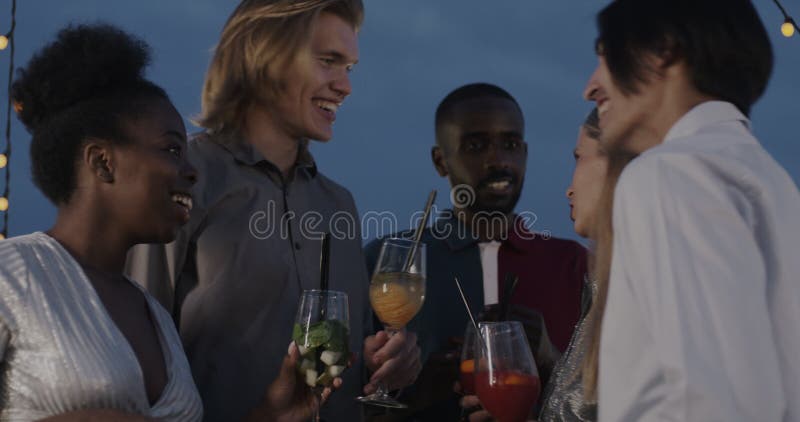 Gruppe von Leuten mit Cocktailbrille, die bei einer Party im Freien lachen und nachts gesellig werden
