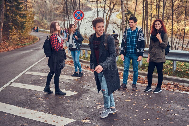 Gruppen av lyckliga vänner av turister står på sidan av vägen och fångar en övergående bil arkivfoto Gruppen av lyckliga vänner av turister står på sidan av vägen och fångar en övergående bil arkivfoto