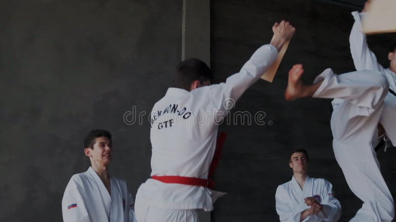 Gruppen av titulTaekwondo manliga sportsmans utför spektakulär original- kampslagställning Grabbar bryter och kraschar träplattan