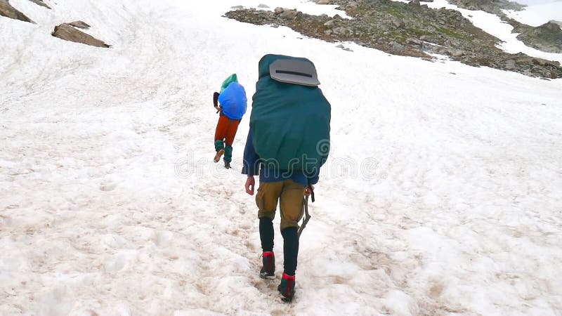Gruppen av turister med att fotvandra ryggsäckar går upp i höga snöig berg