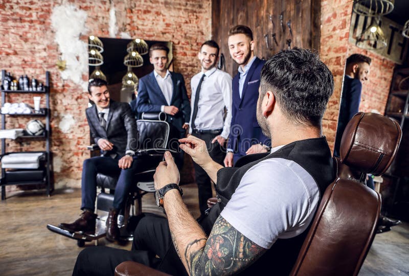 Gruppen av unga eleganta positiva män poserar i inre av frisersalongen arkivfoto Gruppen av unga eleganta positiva män poserar i inre av frisersalongen arkivfoto