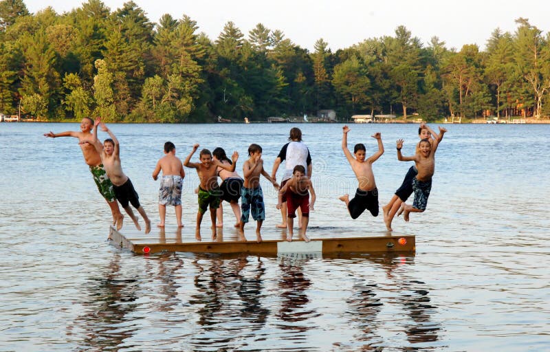 A group of eleven kids ages 11-13 jumping off on a dock into a lake at sumer camp. A group of eleven kids ages 11-13 jumping off on a dock into a lake at sumer camp.