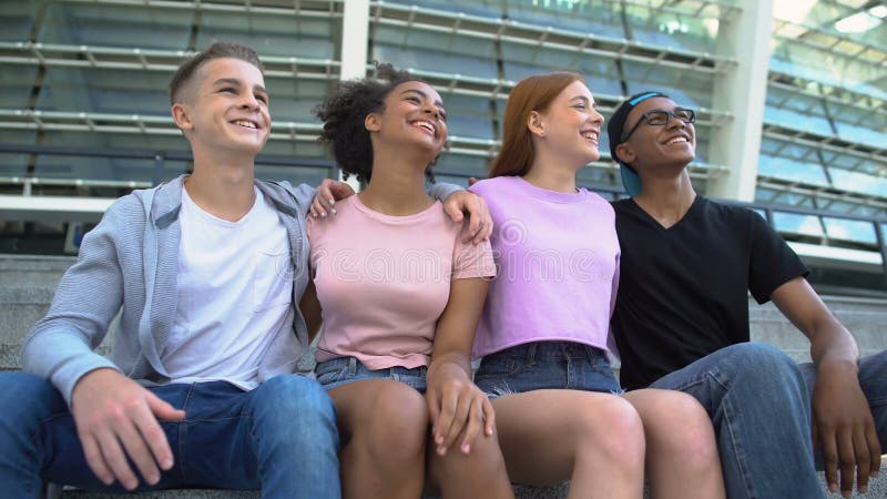 Gruppi multi-razziali di giovani che si abbracciano seduti all'aperto per l'amicizia
