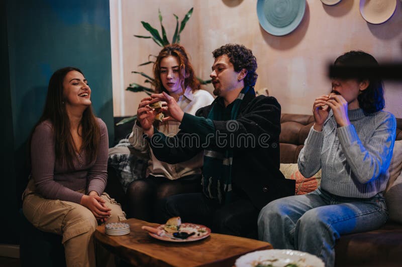 Gruppo di amici che si divertono a mangiare insieme in una saletta accogliente immagine stock