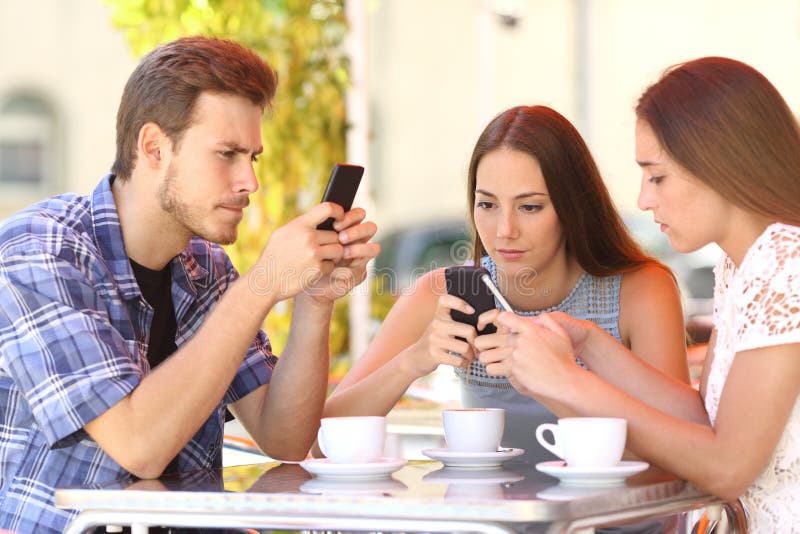 Group of three smart phone addicted friends in a coffee shop terrace everyone with one cellphone. Group of three smart phone addicted friends in a coffee shop terrace everyone with one cellphone