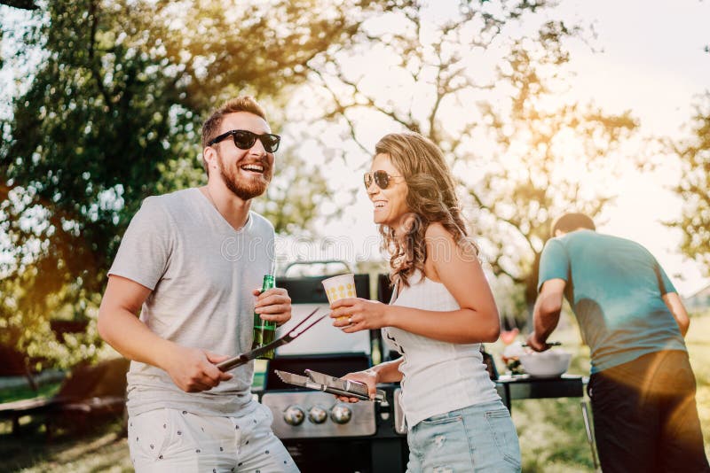 Gruppo di amici sorridenti nella vacanza che mangia le birre e che cucina sul barbecue del giardino Stile di vita, concetto di sv fotografia stock Gruppo di amici sorridenti nella vacanza che mangia le birre e che cucina sul barbecue del giardino Stile di vita, concetto di sv fotografia stock