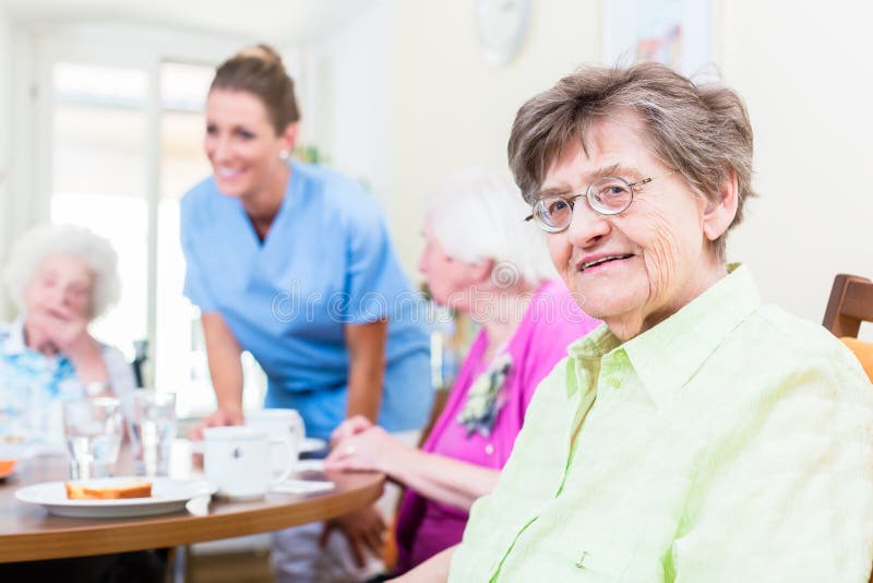 Group of seniors having food in nursing home, a nurse is serving. Group of seniors having food in nursing home, a nurse is serving