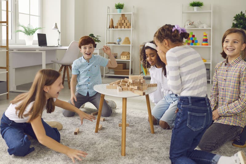 Gruppo di bambini che ridono di una torre a blocchi di legno rotta mentre giocano insieme a stacking board game fotografia stock