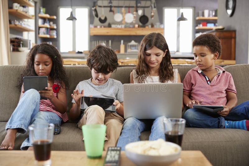 Group Of Children Sitting On Sofa Using Digital Devices. Group Of Children Sitting On Sofa Using Digital Devices