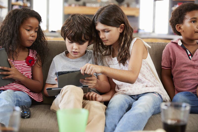 Group Of Children Sitting On Sofa Using Digital Devices. Group Of Children Sitting On Sofa Using Digital Devices