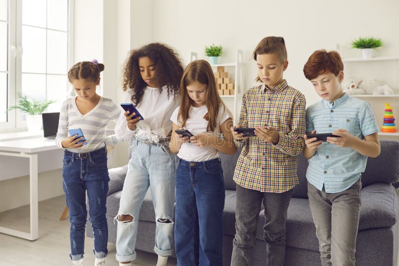 Gruppo di bambini di razza mista in piedi e che giocano o chiacchierano sugli smartphone immagine stock libera da diritti
