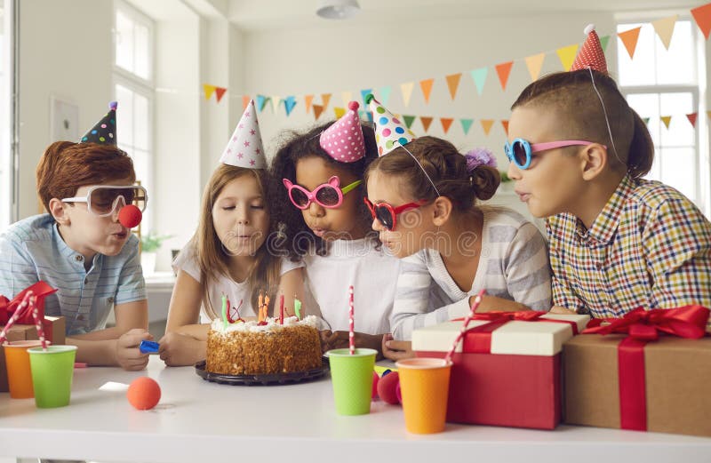 Gruppo di bambini tutti insieme spalmando candele sulla torta di compleanno alla festa di divertimento a casa fotografia stock