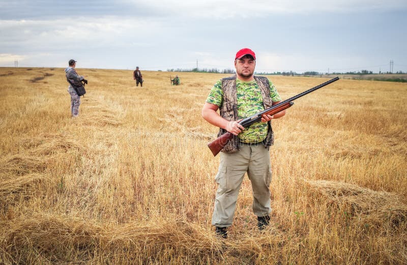 Gruppo di cacciatori con le pistole che si muovono attraverso il campo immagine stock Gruppo di cacciatori con le pistole che si muovono attraverso il campo immagine stock