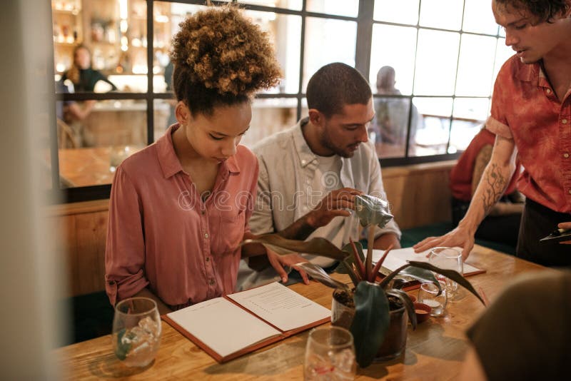 Young women reading through a menu while sitting with a group of friends at a table in a trendy restaurant. Young women reading through a menu while sitting with a group of friends at a table in a trendy restaurant