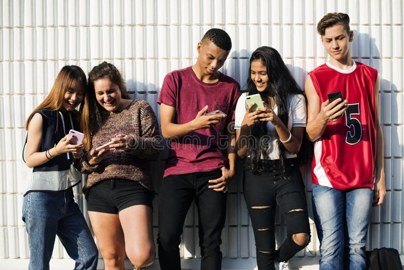 Gruppo di giovani amici dell'adolescente che raffreddano insieme fuori facendo uso del concetto sociale di media dello smartphone