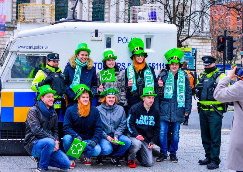 Gruppo di giovani con i cappelli verdi che prendono foto con la polizia a Belfast al giorno del ` s di St Patrick immagini stock Gruppo di giovani con i cappelli verdi che prendono foto con la polizia a Belfast al giorno del ` s di St Patrick immagini stock