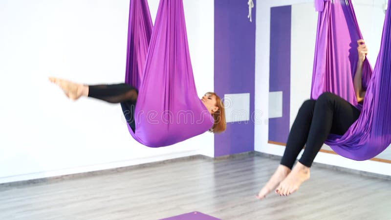 Gruppo di giovani donne che fanno pratica aerea di yoga in amaca porpora