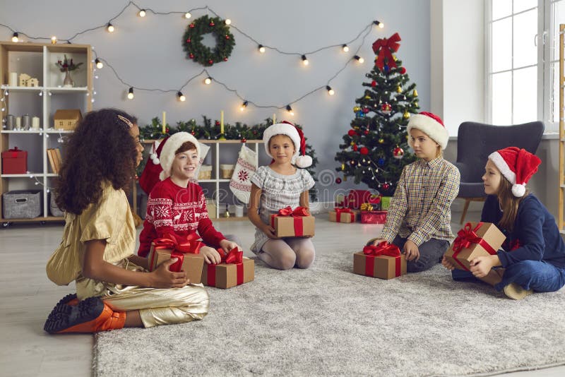 Gruppo di ragazzi seduti per terra con i loro regali e parlano di Natale mattina a casa fotografia stock libera da diritti