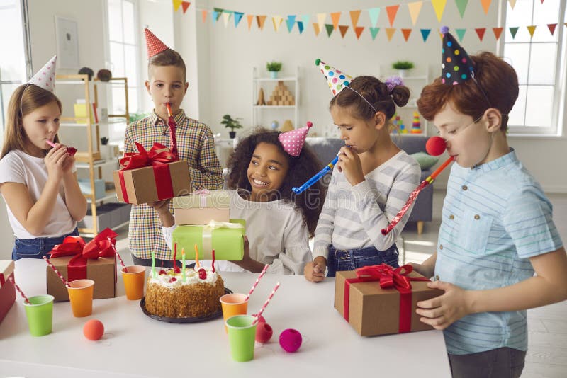 Gruppo di sorridenti bambini di razza mista con fischietti decorativi che fanno festa di compleanno immagine stock libera da diritti