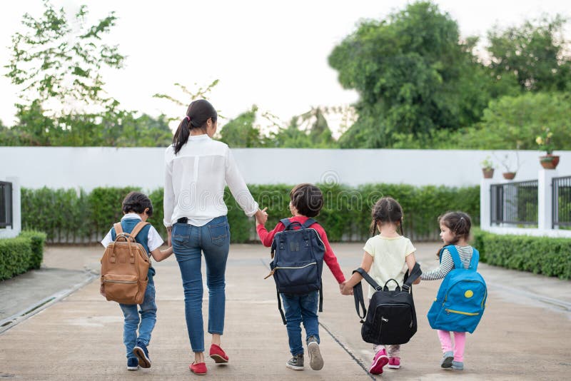 Group of preschool student and teacher holding hands and walking to home. Mom bring her children go to school together. Back to school and Education concept. People and lifestyles theme. Back view. Group of preschool student and teacher holding hands and walking to home. Mom bring her children go to school together. Back to school and Education concept. People and lifestyles theme. Back view