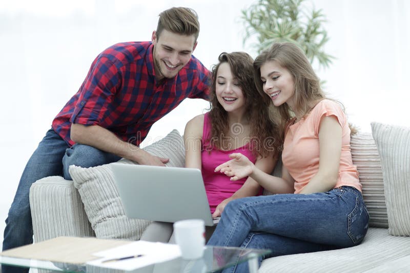 Gruppo di studenti che esaminano uno schermo del computer portatile, sedentesi sullo strato fotografia stock libera da diritti Gruppo di studenti che esaminano uno schermo del computer portatile, sedentesi sullo strato fotografia stock libera da diritti