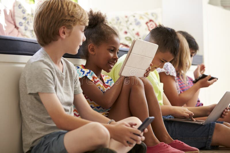 Group Of Children Sit On Floor And Use Technology. Group Of Children Sit On Floor And Use Technology