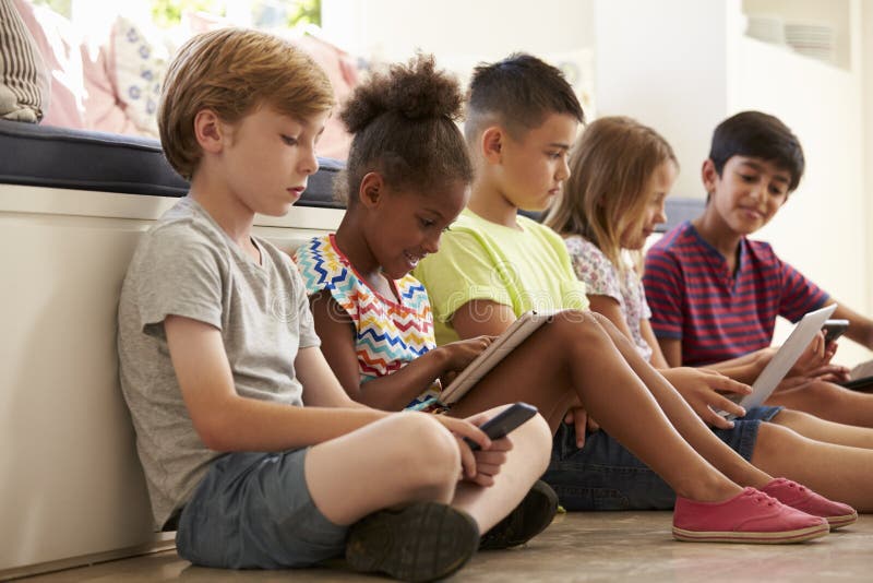 Group Of Children Sit On Floor And Use Technology. Group Of Children Sit On Floor And Use Technology