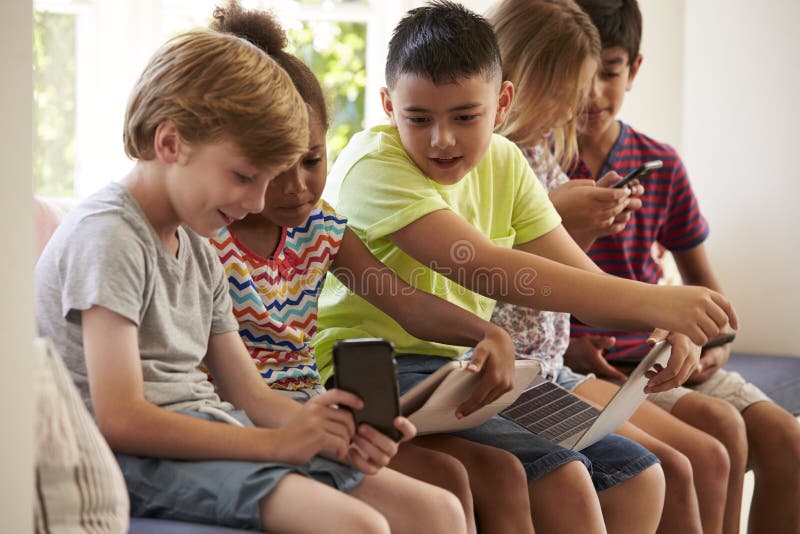 Group Of Children Sit On Window Seat And Use Technology. Group Of Children Sit On Window Seat And Use Technology