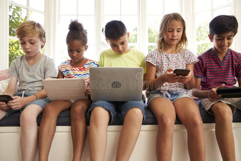 Group Of Children Sit On Window Seat And Use Technology. Group Of Children Sit On Window Seat And Use Technology