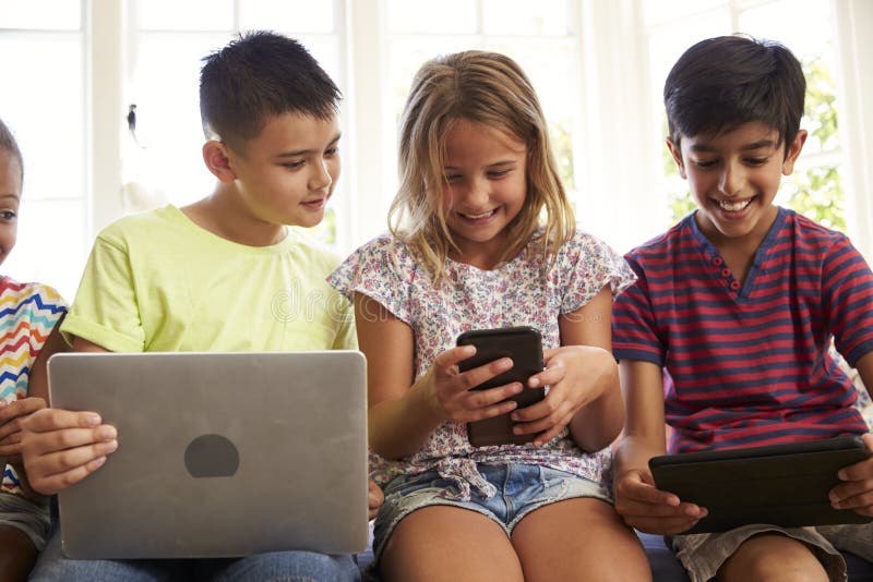 Group Of Children Sit On Window Seat And Use Technology. Group Of Children Sit On Window Seat And Use Technology