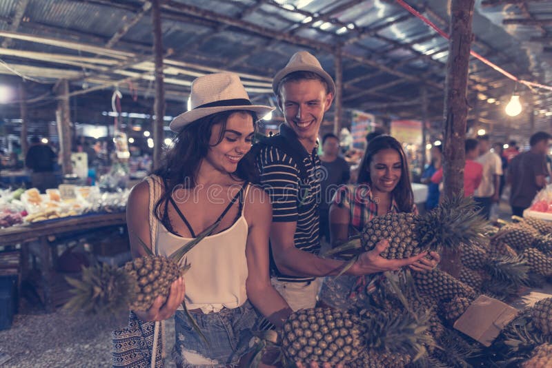 Gruppo di turisti che scelgono ananas sul mercato di strada tropicale nei giovani allegri della Tailandia che comprano frutta fre immagine stock libera da diritti Gruppo di turisti che scelgono ananas sul mercato di strada tropicale nei giovani allegri della Tailandia che comprano frutta fre immagine stock libera da diritti