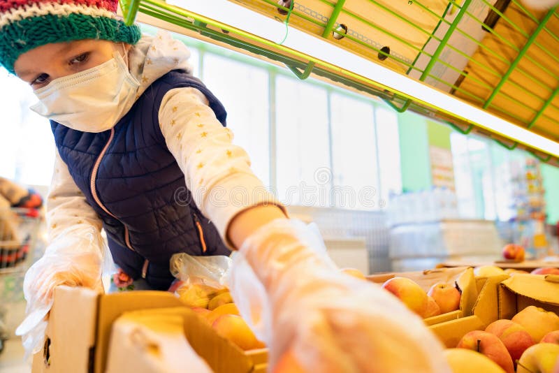 Kid girl in a medical mask and gloves making purchases in the store, choose apples. epidemic and quarantine. protection from viruses. Kid girl in a medical mask and gloves making purchases in the store, choose apples. epidemic and quarantine. protection from viruses.