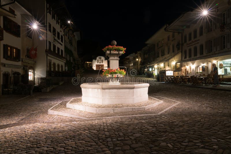 Gruyeres, VD/Suiza - 31 de mayo de 2019: el pueblo medieval histórico de Gruyeres con la fuente cuadrada del pueblo en la noche imagen de archivo libre de regalías Gruyeres, VD/Suiza - 31 de mayo de 2019: el pueblo medieval histórico de Gruyeres con la fuente cuadrada del pueblo en la noche imagen de archivo libre de regalías