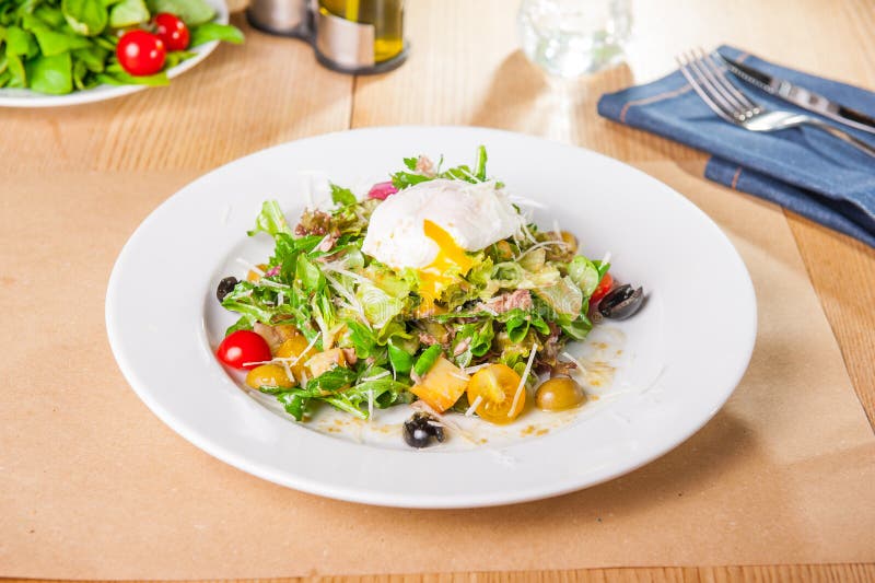 Grön grönsaksallad med tonfisk och det tjuvjagade ägget på den vita plattan på den trätjänade som tabellen Selektiv fokus, kopier royaltyfri bild Grön grönsaksallad med tonfisk och det tjuvjagade ägget på den vita plattan på den trätjänade som tabellen Selektiv fokus, kopier royaltyfri bild