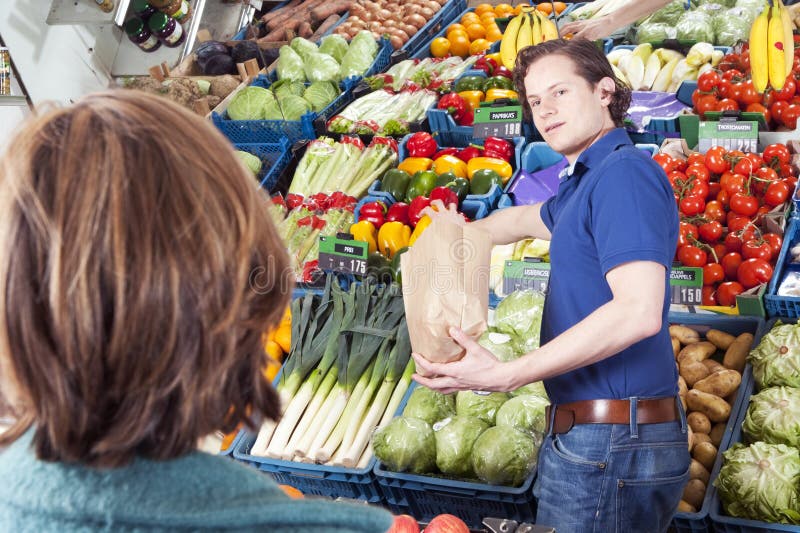 Green grocer serving a customer, filling a brown paper bag with peppers. Green grocer serving a customer, filling a brown paper bag with peppers